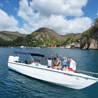 Group of people on a boat waving, with lush hills and cloudy sky in the background.