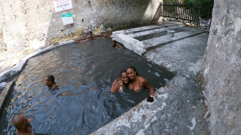 People enjoying a hot spring pool surrounded by stone walls and greenery.