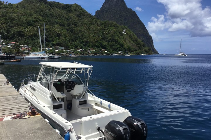 White speedboat docked with lush hills and a distant peak in the background.