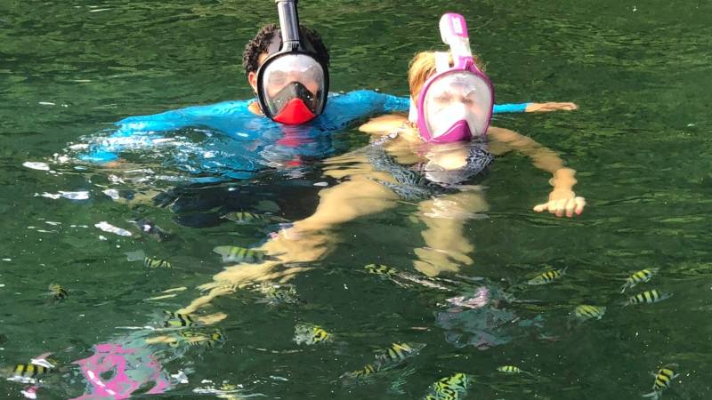Two people snorkeling in clear water with colorful fish visible below.