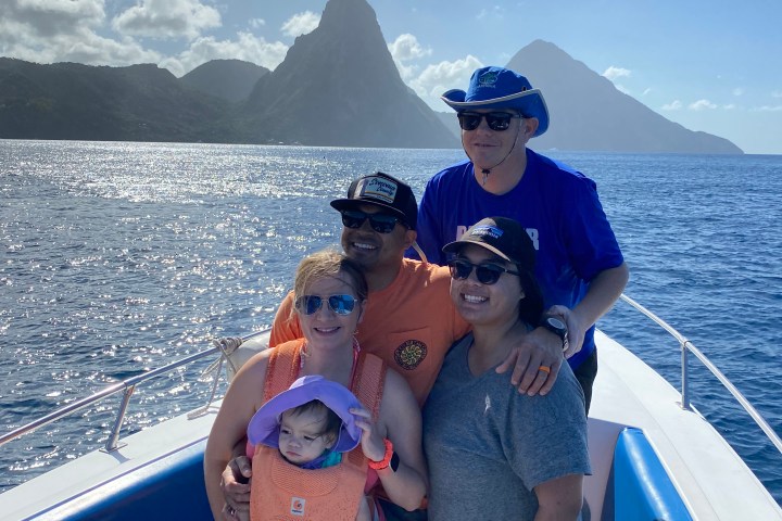 Group of five on a boat with mountains and ocean in the background.