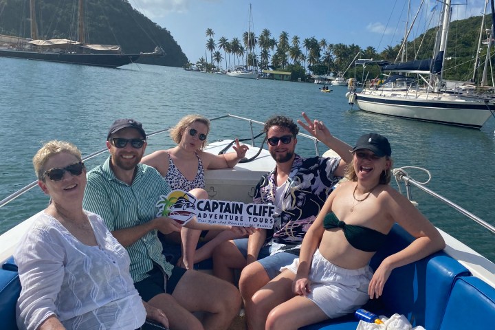 Group of five people smiling on a boat with a 'Captain Cliff Adventure Tours' sign.