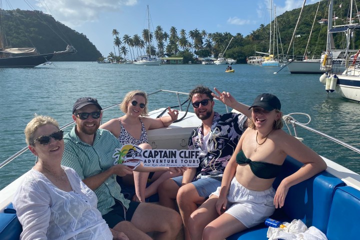 Group of people on a boat with 'Captain Cliff Adventure Tours' sign, surrounded by water and palm trees.