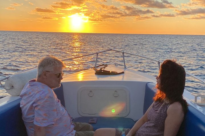 Two people sitting on a boat, watching a sunset over the ocean.