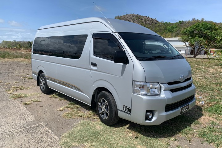 Silver van parked on a grassy dirt area with a hill and trees in the background.
