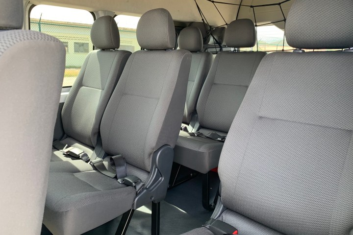Interior of a passenger van with rows of gray fabric seats and seat belts.