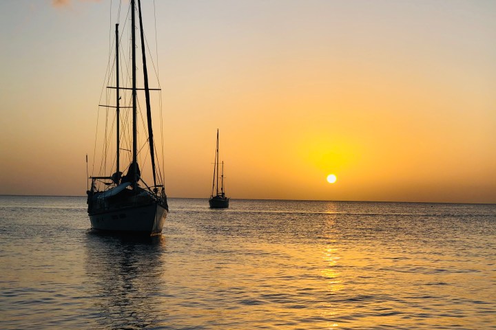 Two sailboats on calm water during sunset with a golden sky.