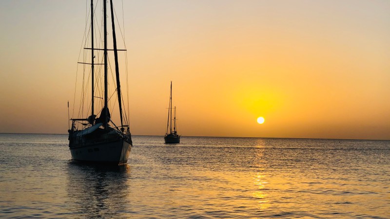 Two sailboats on calm water during sunset with a golden sky.