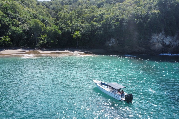 Boat on turquoise water near a forested shoreline with a sandy beach.